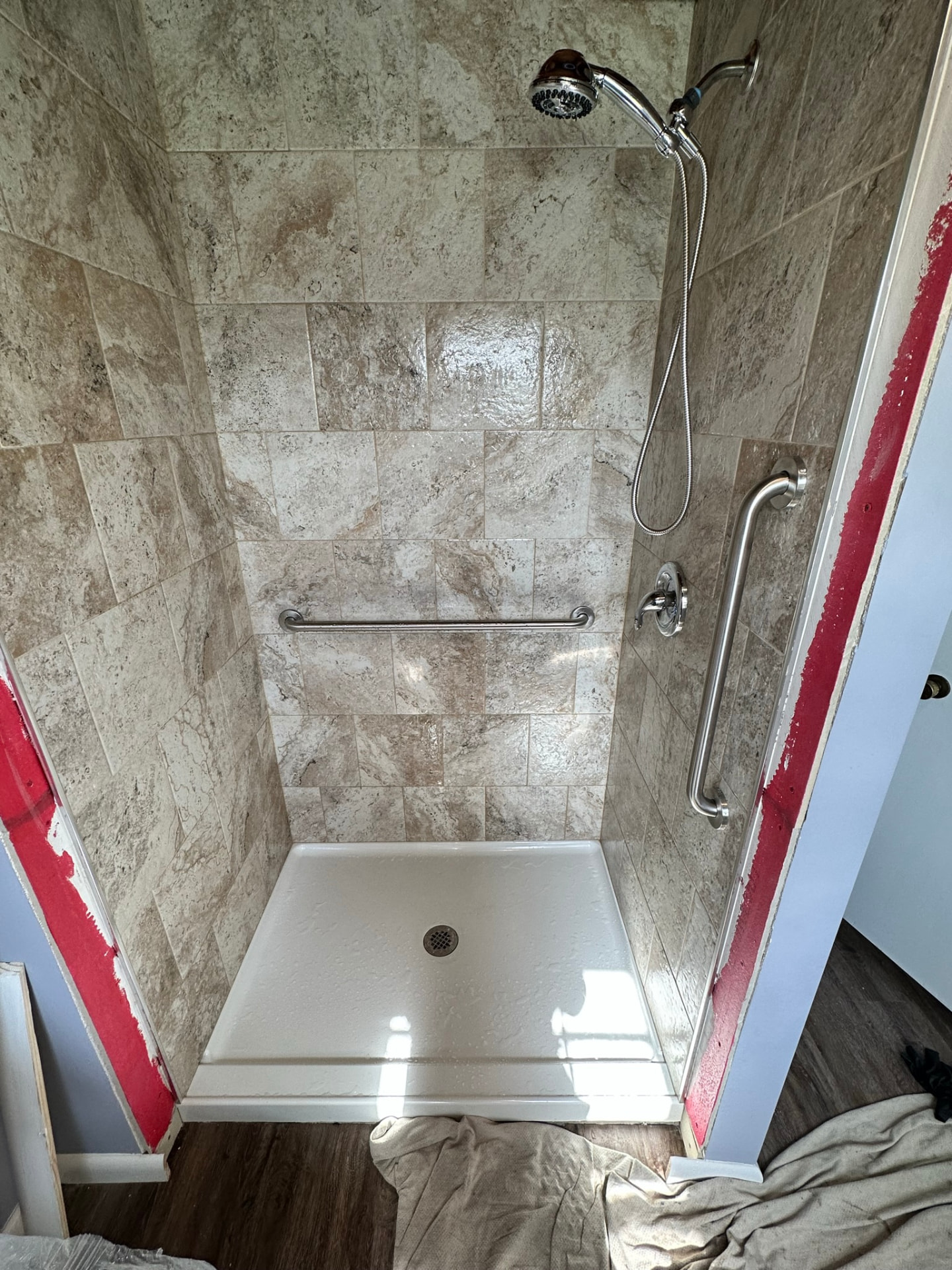 Newly installed shower pan with tile surround, grab bars and shower valve