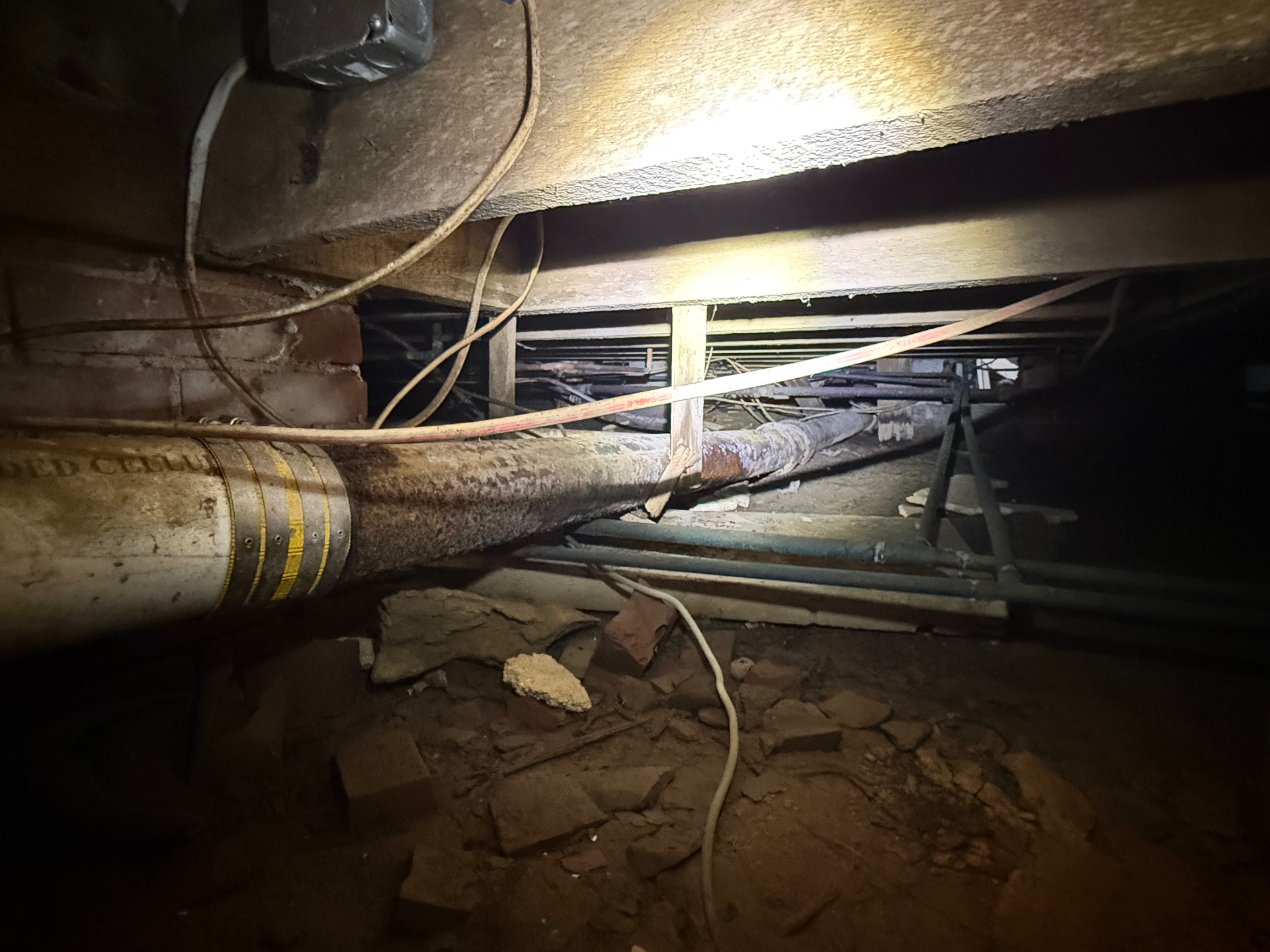Old cast iron main drain line running under floor joists in a Madison crawlspace
