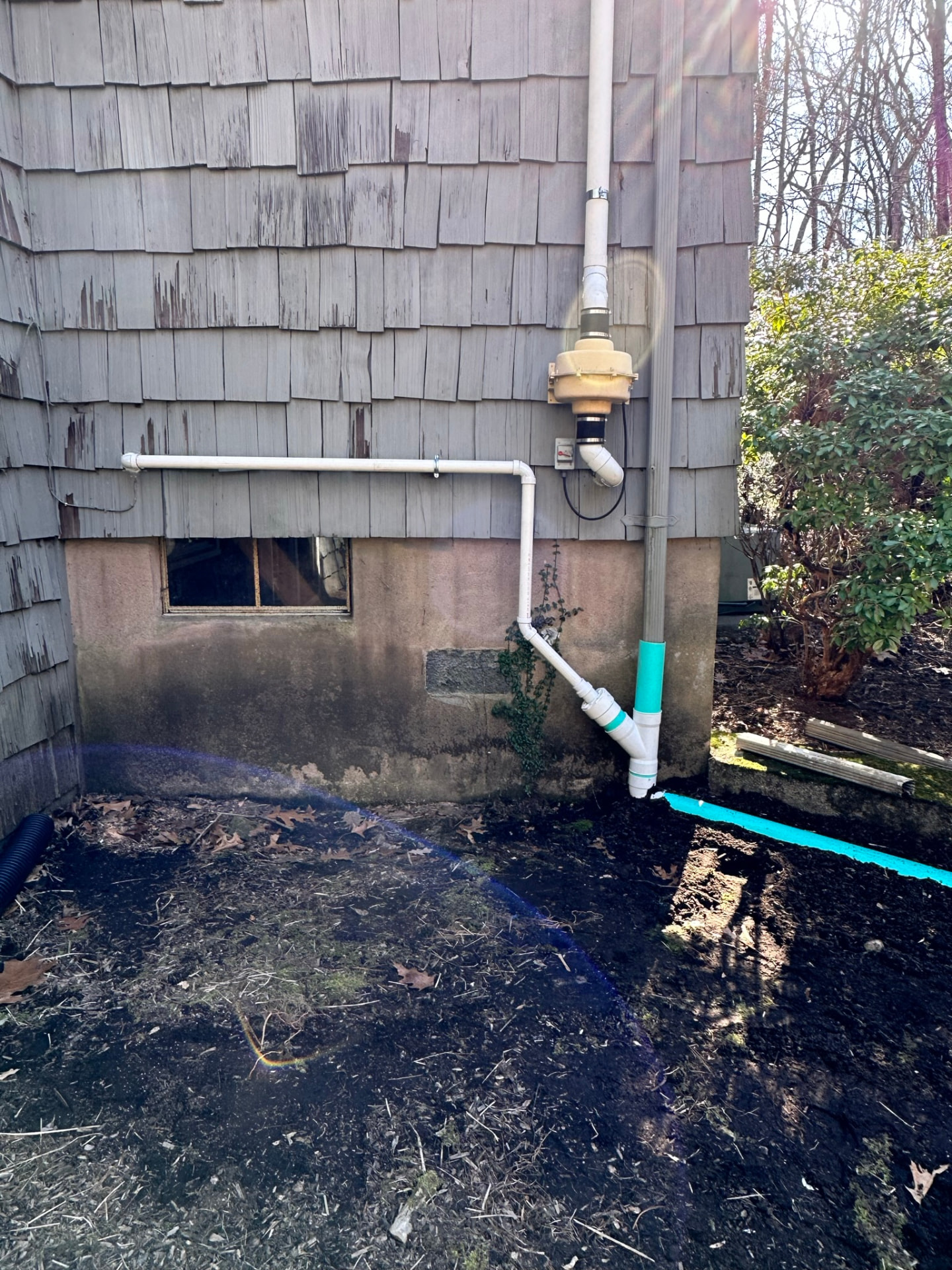 Exterior sump discharge with backflow device tied into buried drainage away from the foundation