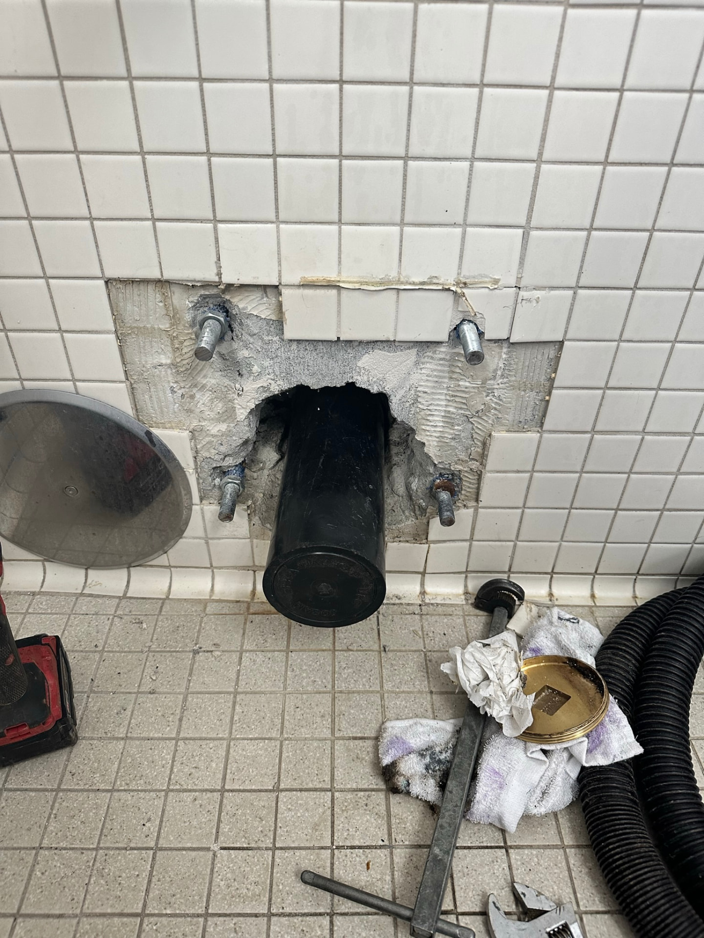 Commercial wall-hung toilet removed exposing the carrier and waste opening in tile wall