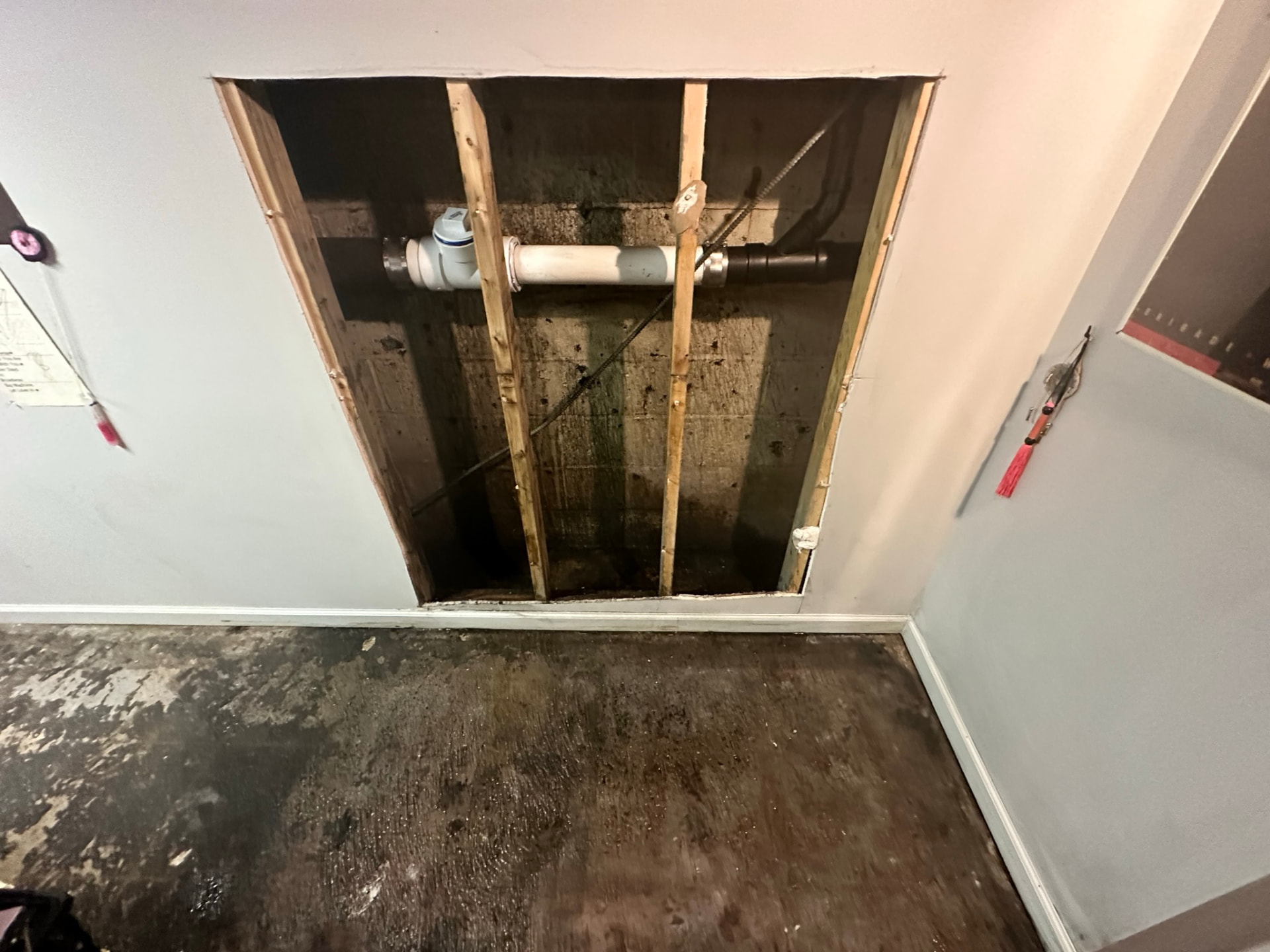 Basement wall opened to expose a water service line and shutoff behind finished drywall