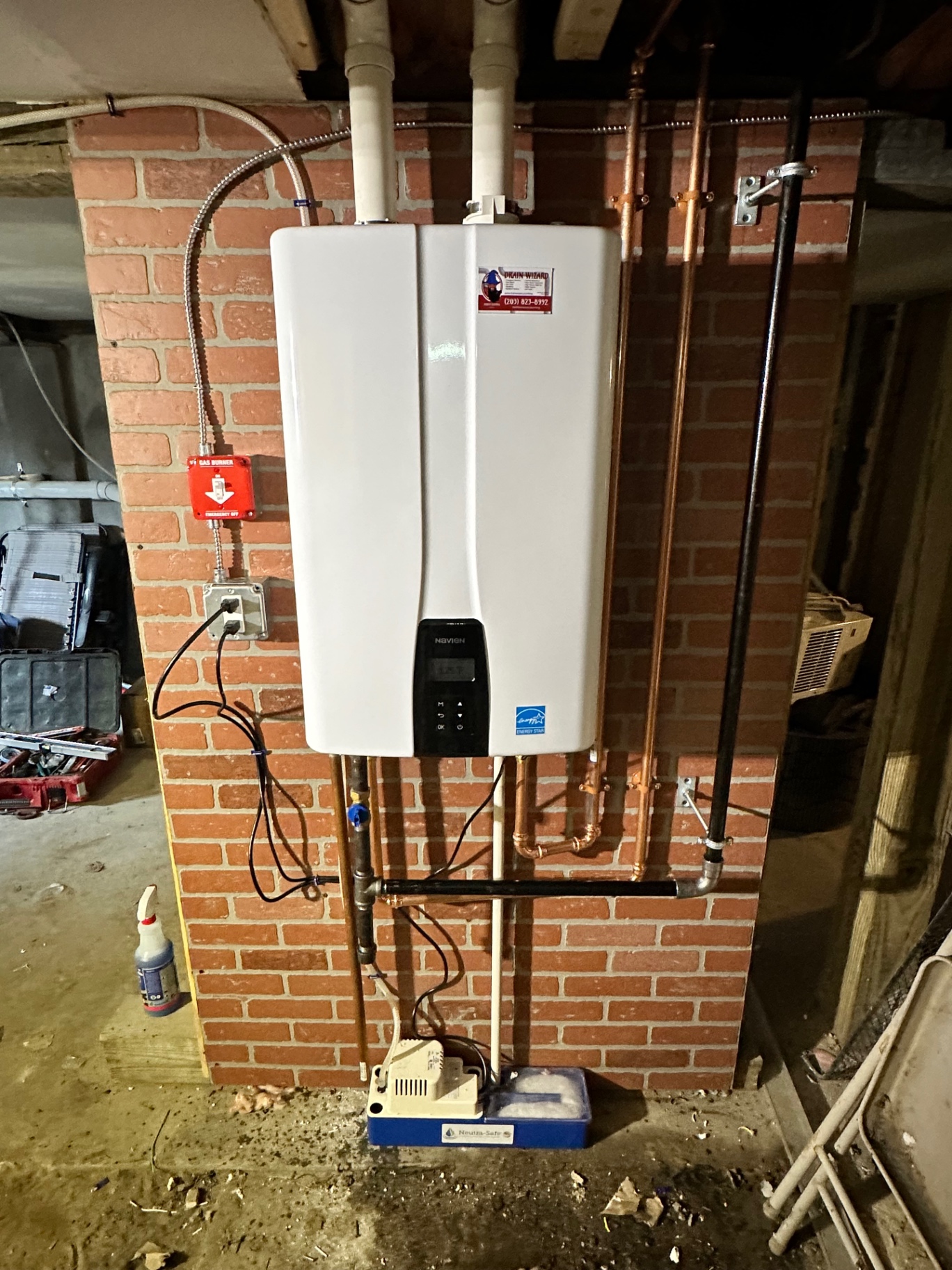 Navien tankless combi unit mounted on a brick chimney wall — energy-star rated, powering both domestic hot water and hydronic heat from a single appliance.