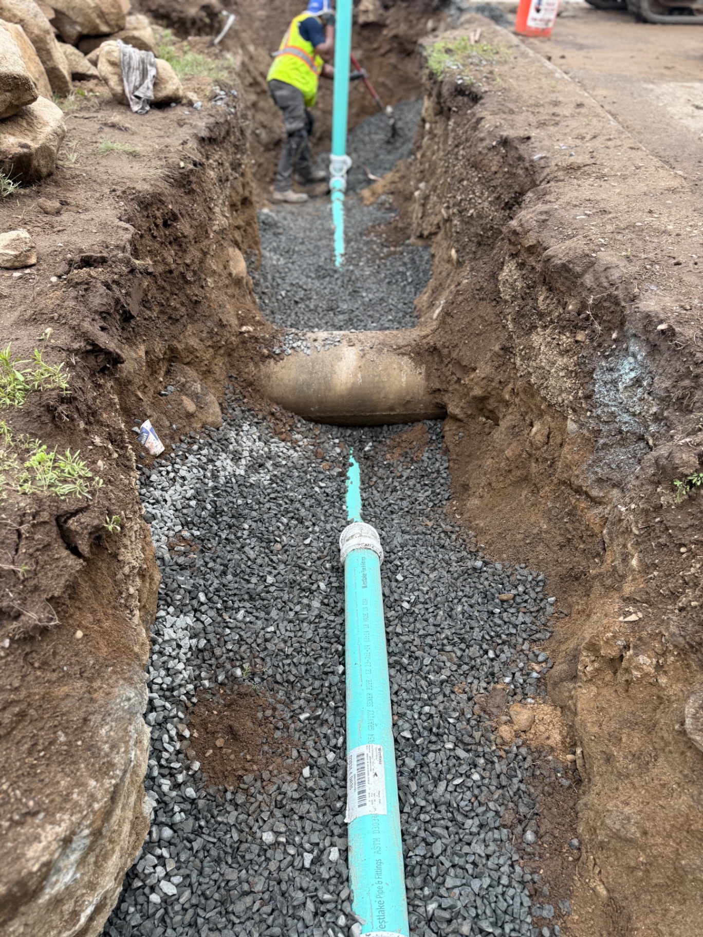 New green PVC gravity sewer pipe seated on a clean bed of 3/4" crushed stone — proper bedding is what keeps the line from settling, cracking, or bellying for decades to come.
