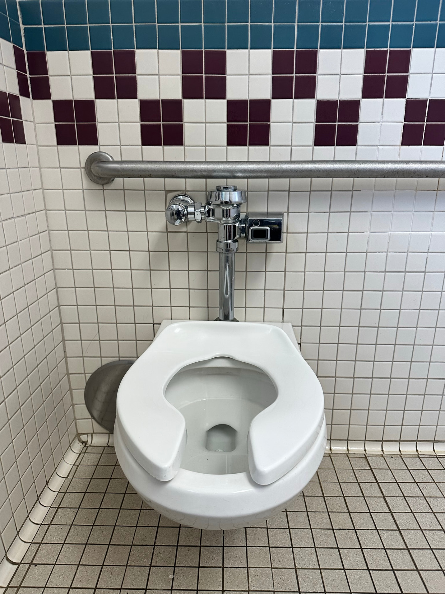 New commercial wall-hung toilet with flushometer installed in a tiled restroom