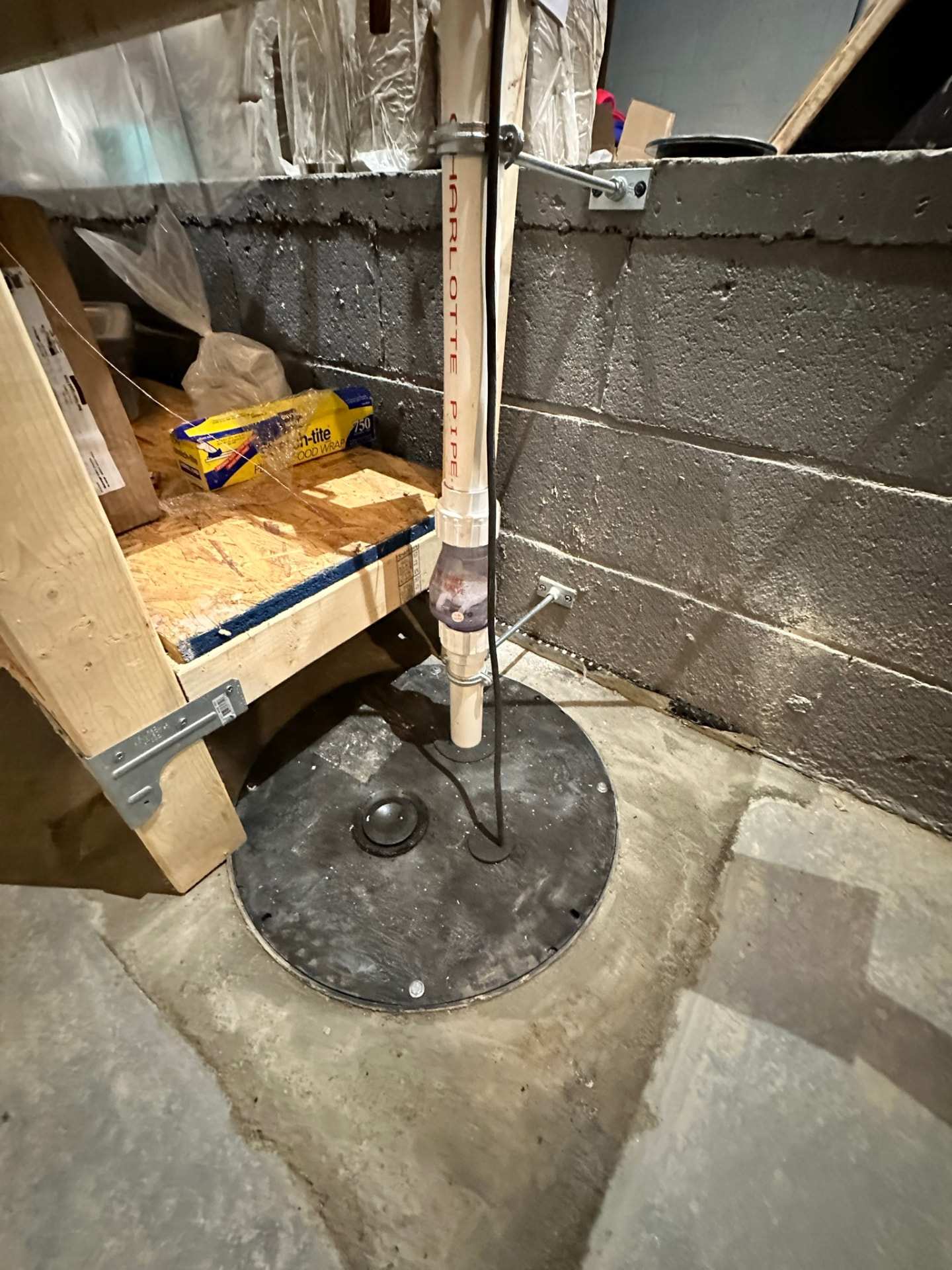 Sealed sump pit lid and strapped PVC discharge line against a block foundation wall