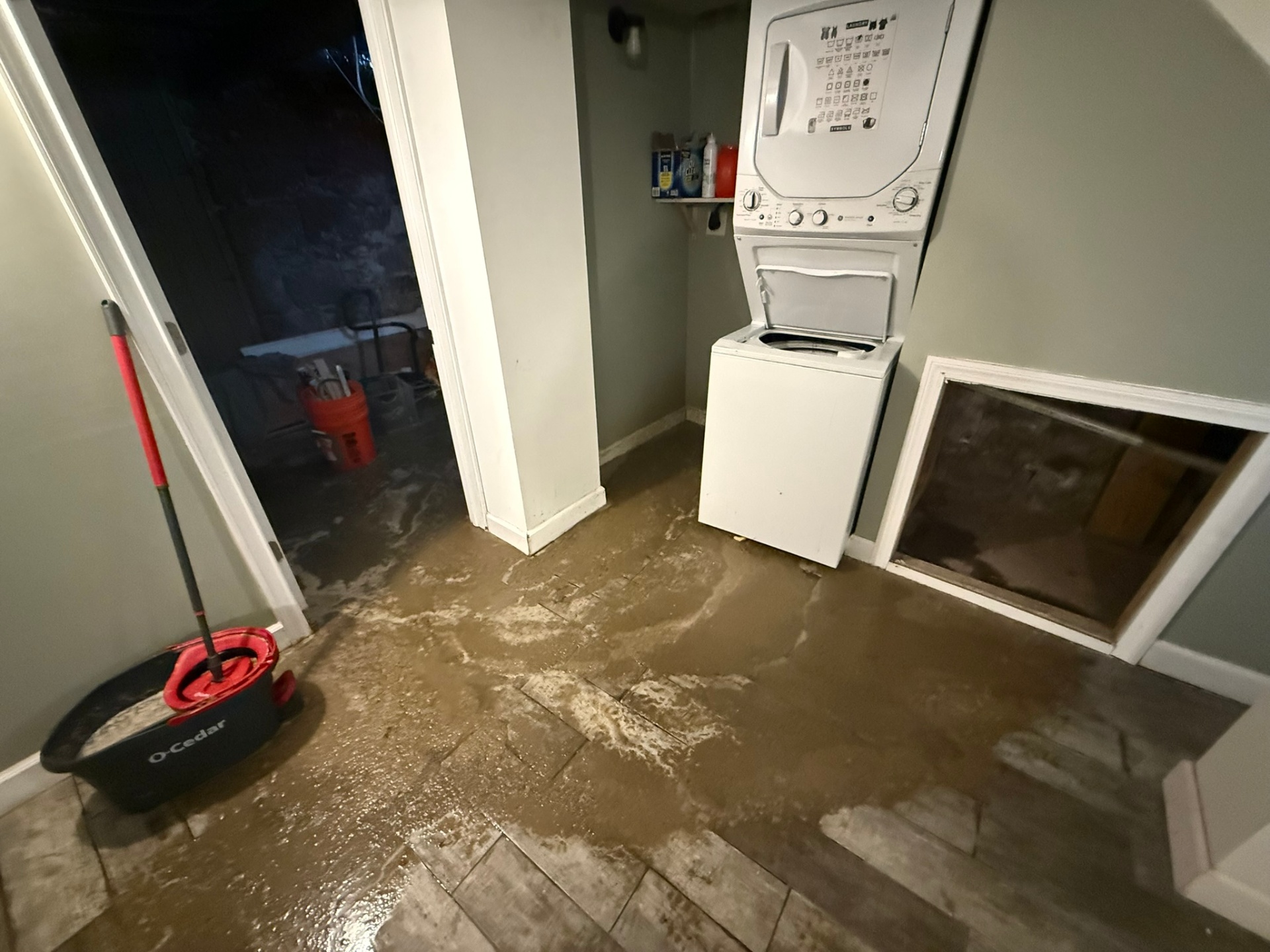 Mud and sediment tracked through a finished basement laundry area after a storm-driven flood event — full muck-out and sanitization required before drying.