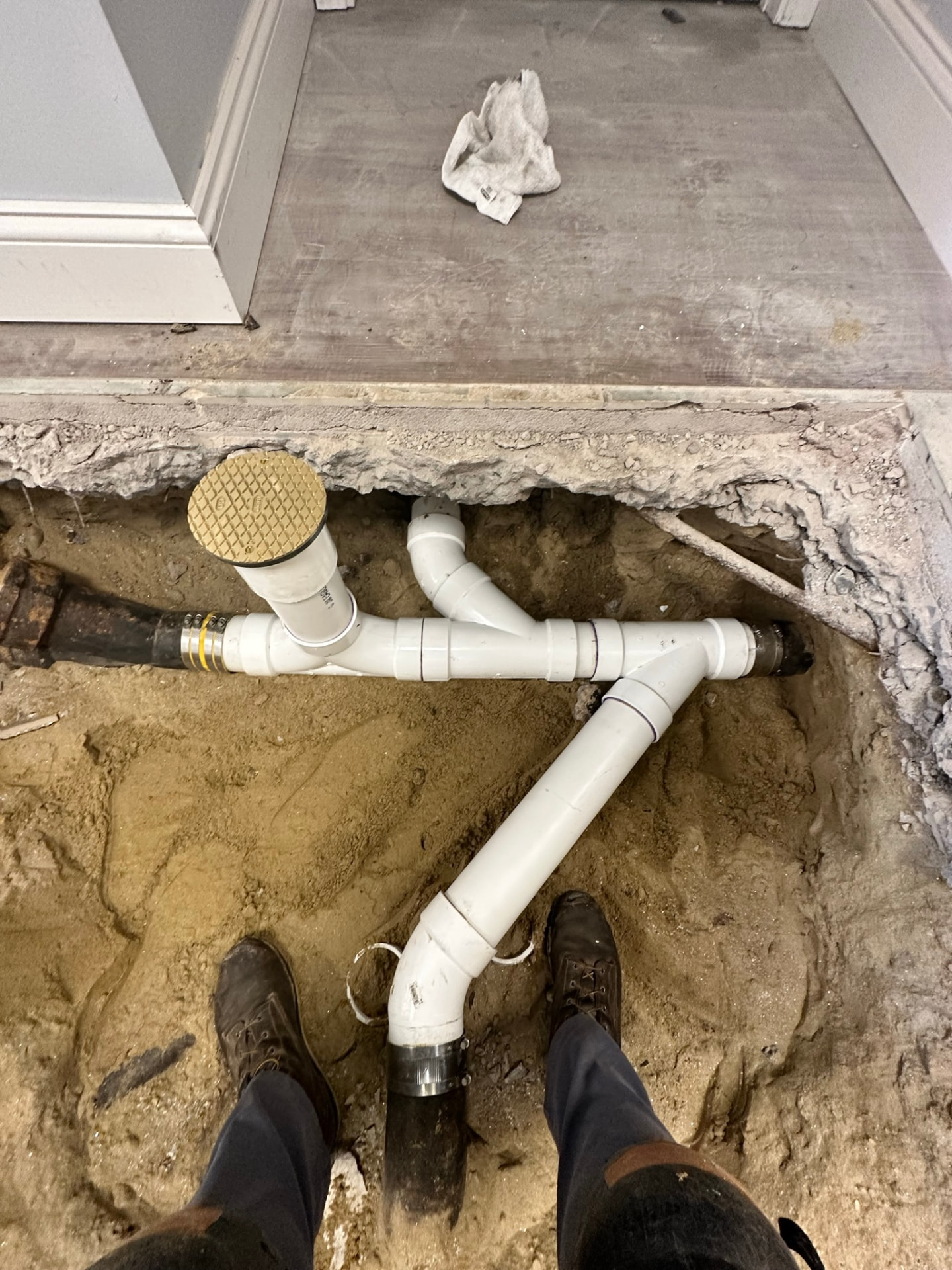 New PVC drain line and cleanout with brass cover installed in an opened slab trench