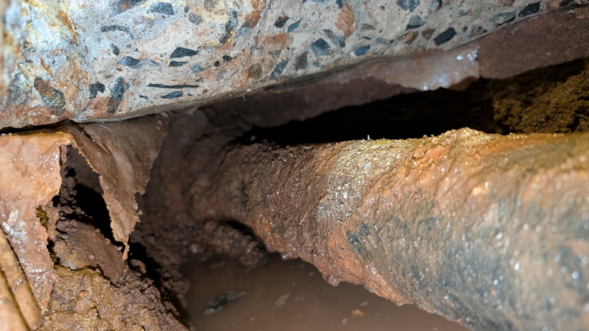 Close-up of the failure — the underside of the cast iron has rotted through, dumping waste and water directly into the soil beneath the slab.