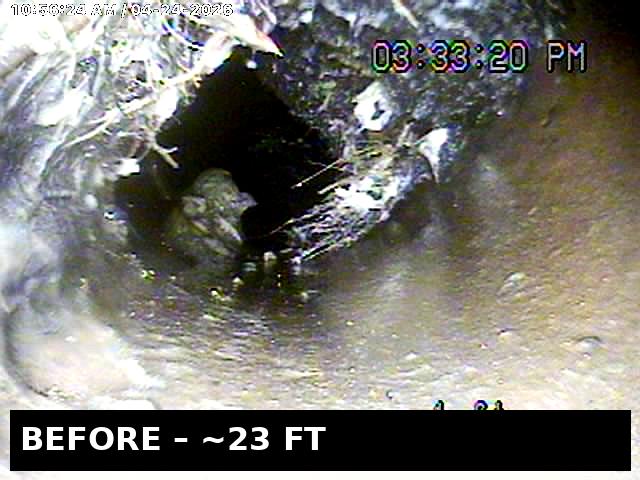 BEFORE — 23 ft down the sewer lateral: massive root ball invading the pipe through a cracked joint, choking flow to a trickle. Camera doesn't lie.