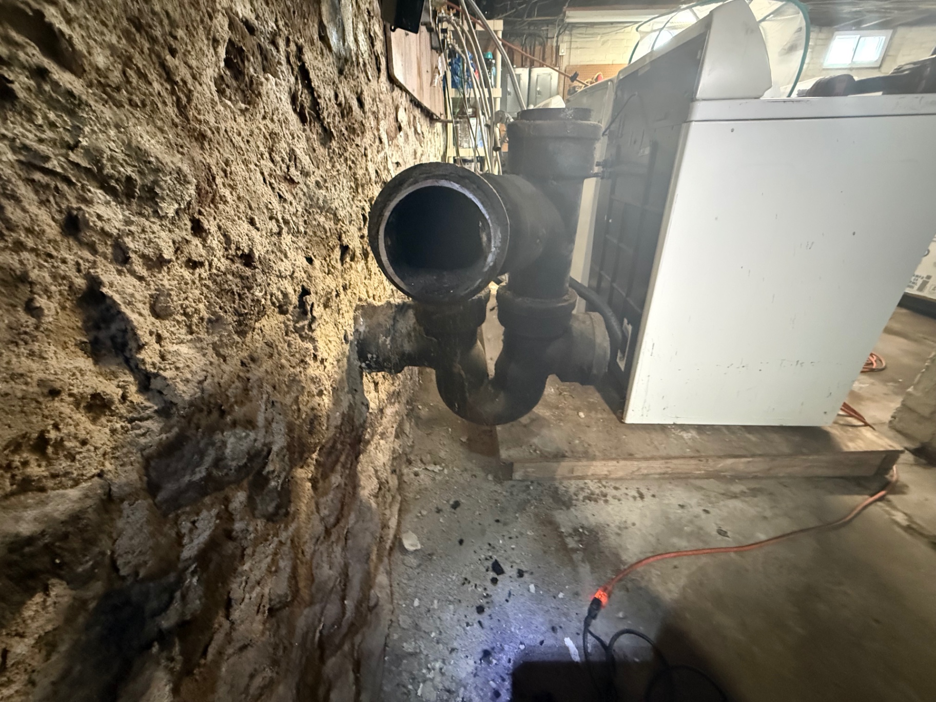 Basement plumbing area with an open cast-iron drain pipe beside an appliance in a Wallingford home