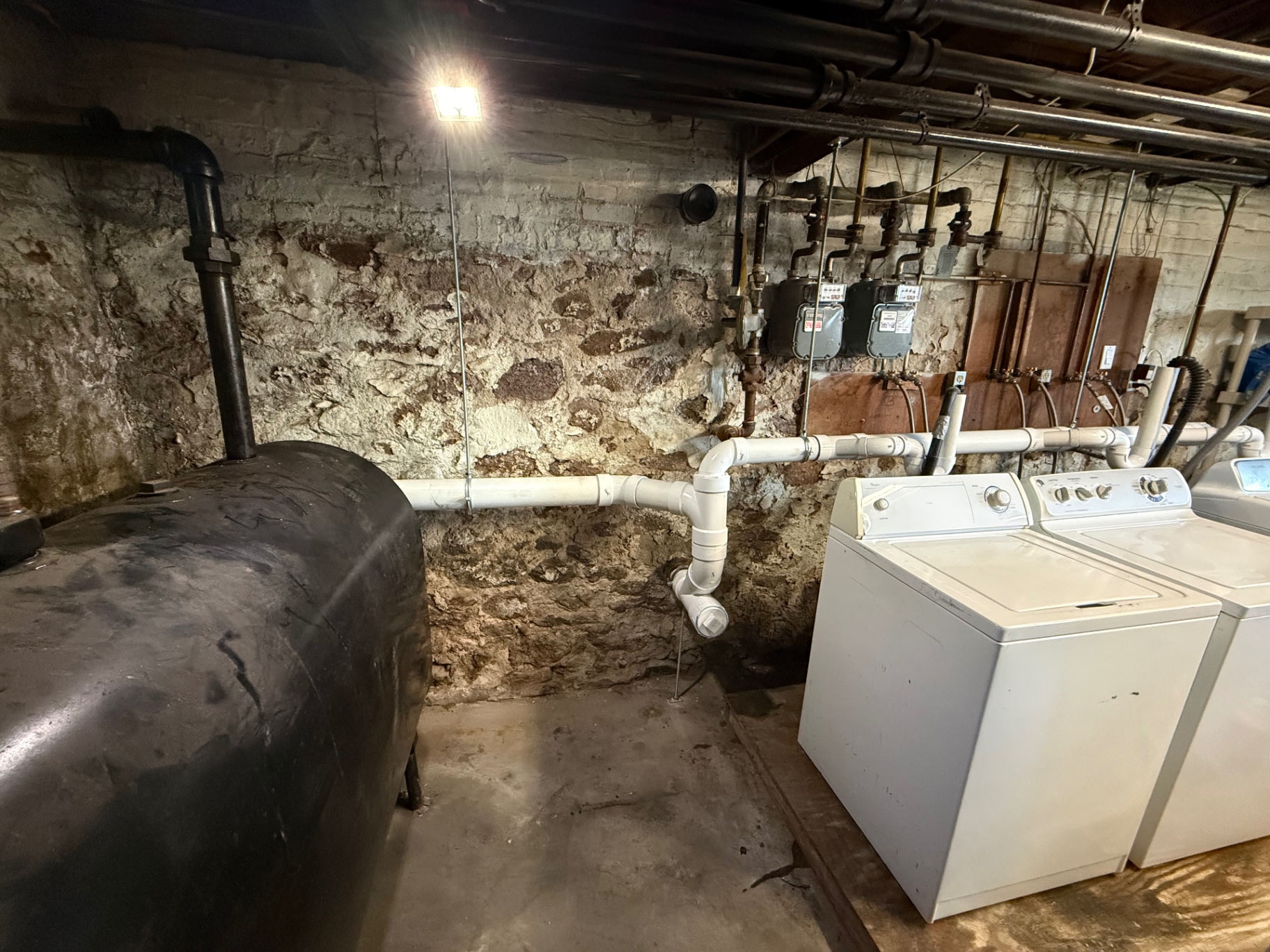 Stone-foundation basement with new white PVC piping, laundry appliances, and gas meters in Wallingford